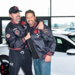 Christian Gudegast and Gerard Butler smile while posing with a Porsche Taycan ahead of their movie Den of Thieves 2: Pantera