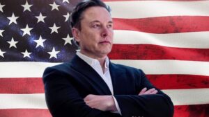 Elon Musk stands in front of an American flag.