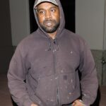 Kanye West wearing a brown hoodie and baseball cap.