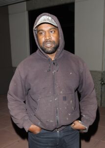 Kanye West wearing a brown hoodie and baseball cap.