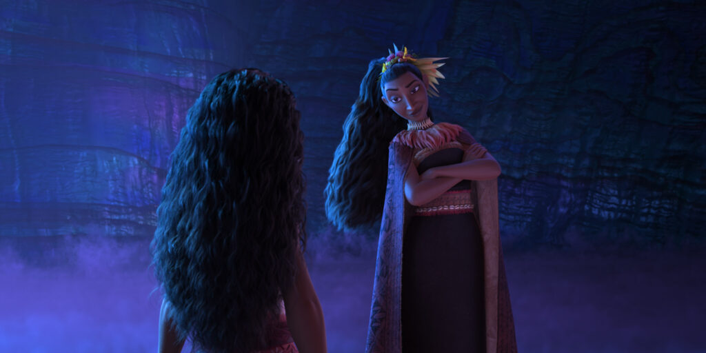 A tall woman with long dark hair in a high ponytail looks at Moana, with her arms crossed over her chest