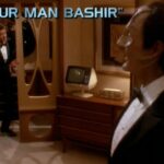 Julian Bashir and Elim Garak stand around in a cool mid-century hotel room (on the holodeck) wearing tuxedos. The title card “Our Man Bashir” is visible.