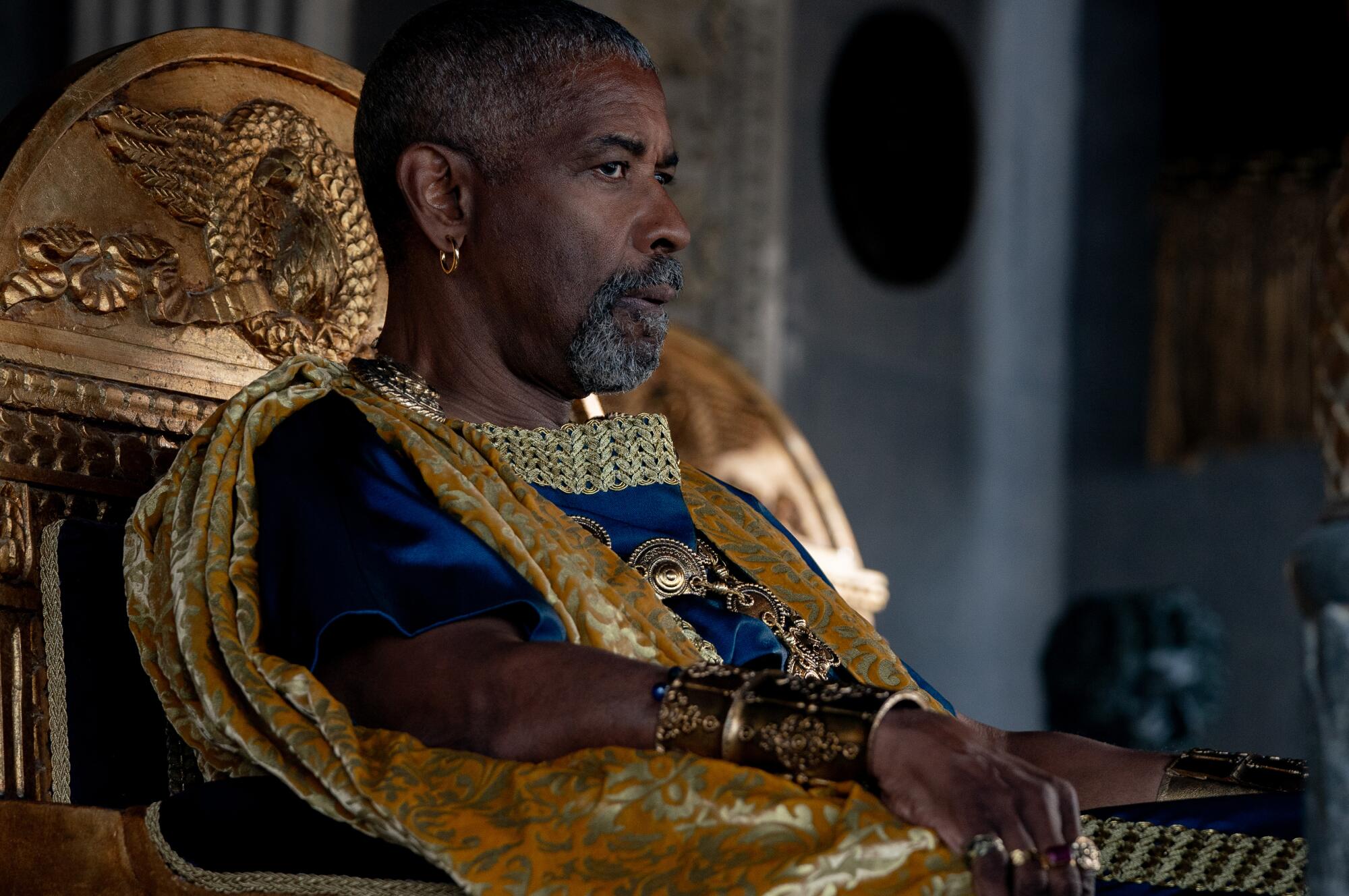 Denzel Washington sits in a golden chair and wears Roman-era finery in a scene from "Gladiator II."