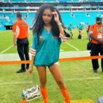 Woman in Miami Dolphins jersey and orange boots at a football stadium.