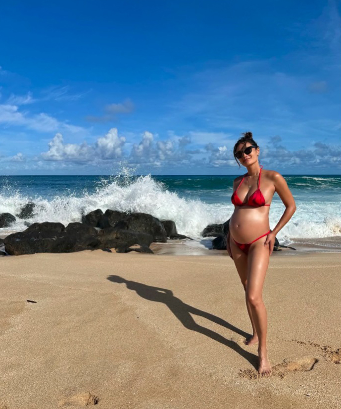 Pregnant woman in red bikini on beach.