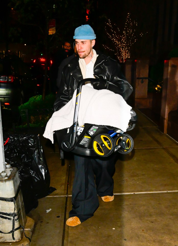 Justin Bieber carrying a baby in a stroller at night.