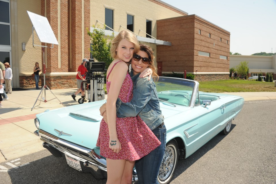 Taylor Swift and Shania Twain hugging in front of a light blue car.