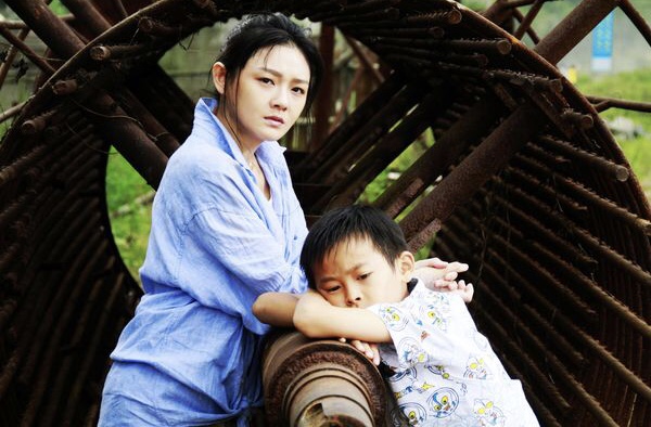 A woman and a young boy rest their arms on a rusty metal structure.