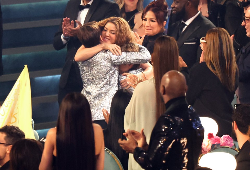 Shakira hugging two people after winning a Grammy award.