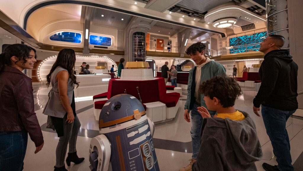 A kid talking to the droid SK-62O in the atrium of the Halcyon