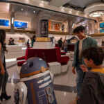 A kid talking to the droid SK-62O in the atrium of the Halcyon