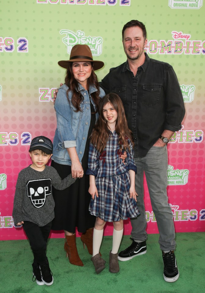 a family poses on a green carpet in front of a disney zombies 2 poster