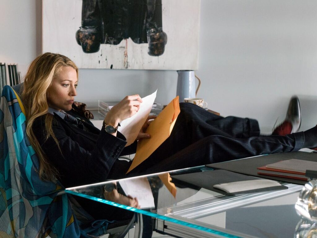 A blond woman reads a document at a desk.