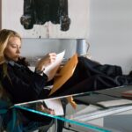 A blond woman reads a document at a desk.