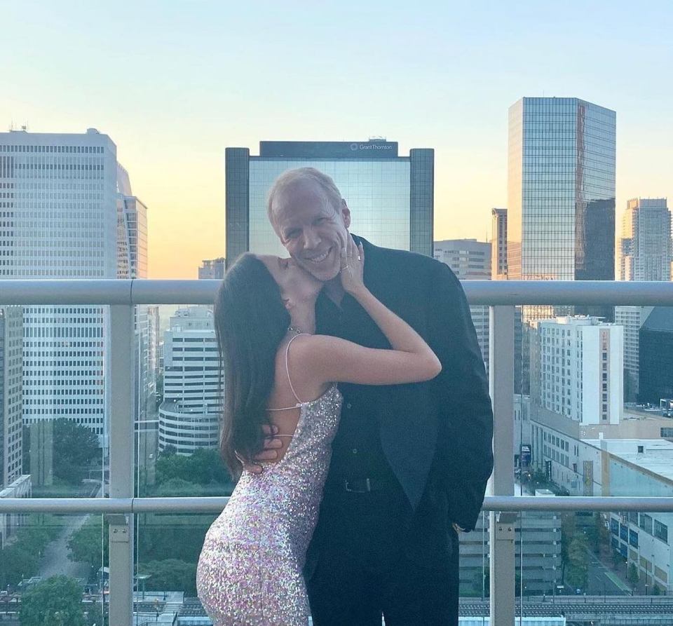 A man and woman embracing on a balcony overlooking a city skyline.