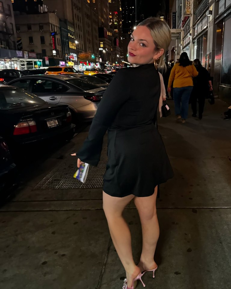 Ella Stiller in a black dress on a city street at night.