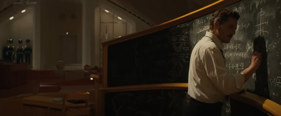 Man writing equations on a large chalkboard.