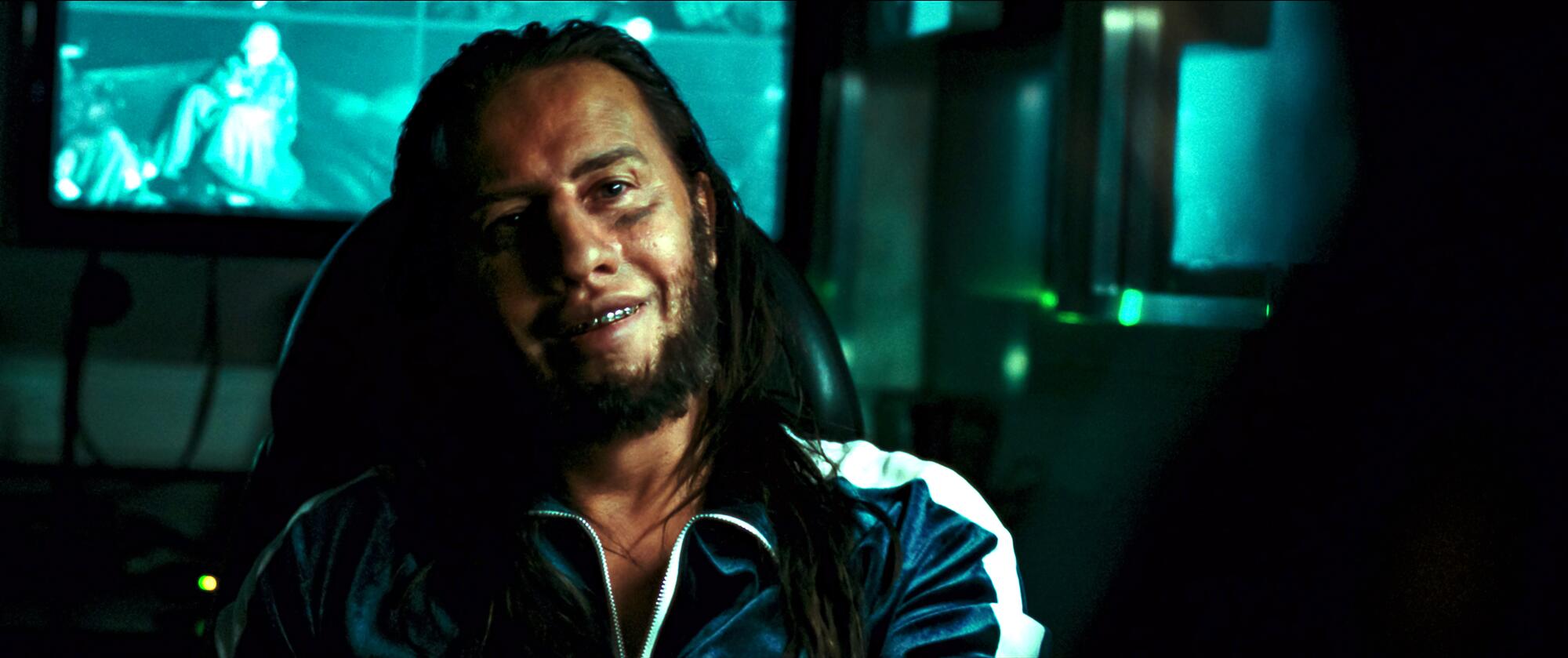 A man with long hair and metal teeth in a scene from "Emilia Perez."