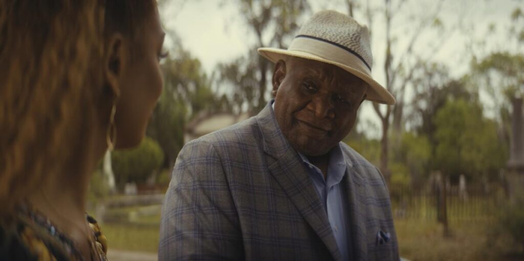 A man in a straw hat and plaid blazer smiles as he looks at a woman.