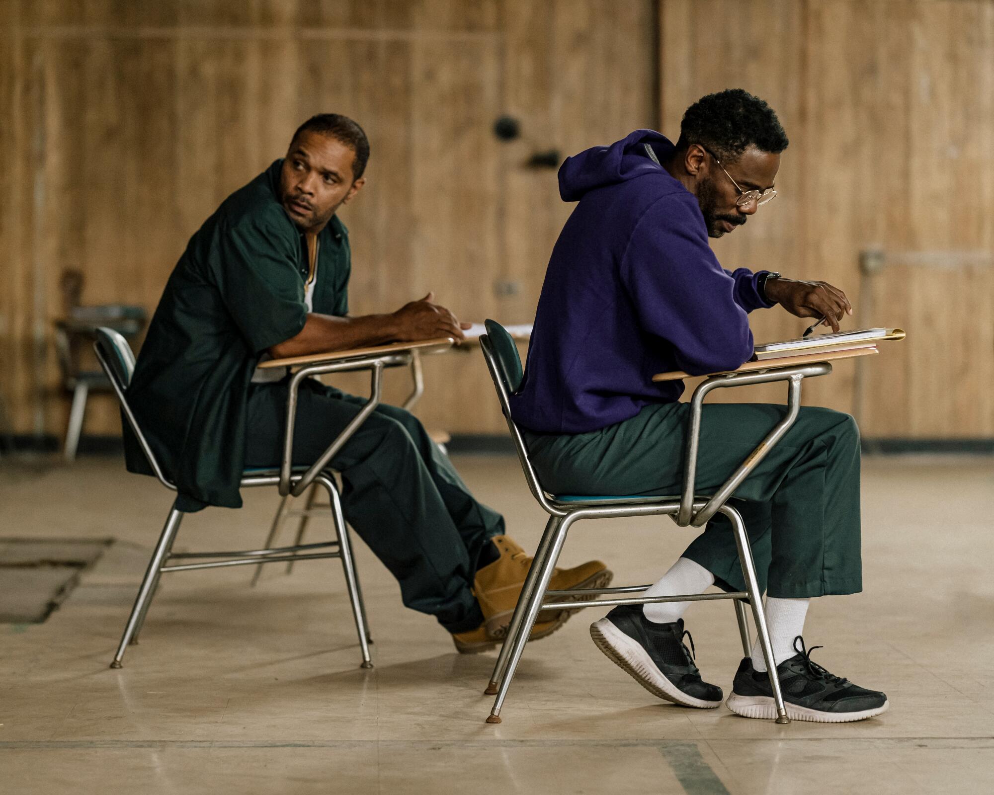 Two men sit at school desks in "Sing Sing."