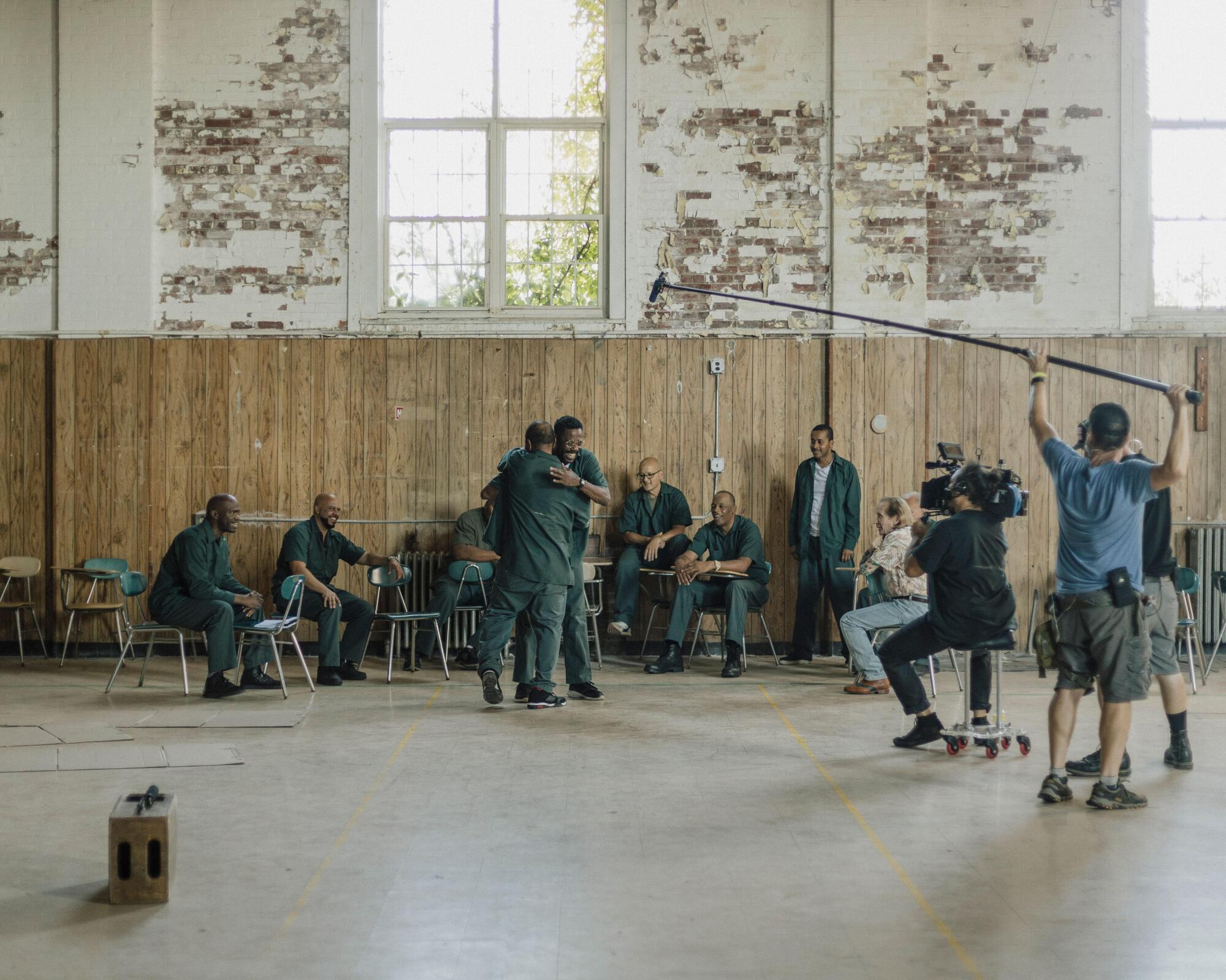 A behind-the-scenes moment on set when two men in prison uniforms hug as others sit watching.