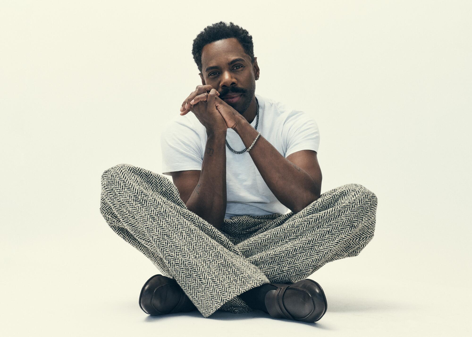 Colman Domingo sits crosslegged on the floor, elbows resting on lifted knees and chin resting on clasped hands.