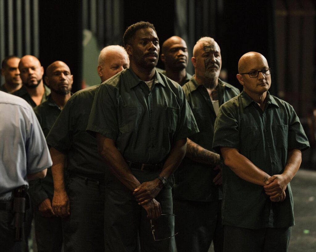 A group of men in prison uniforms stand with hands clasped in "Sing Sing."