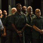 A group of men in prison uniforms stand with hands clasped in "Sing Sing."