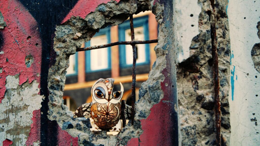 A folkloric miniature of an owl sits in a blown-out wall of a building.