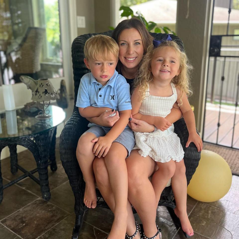 Woman sitting on a chair with two young children on her lap.