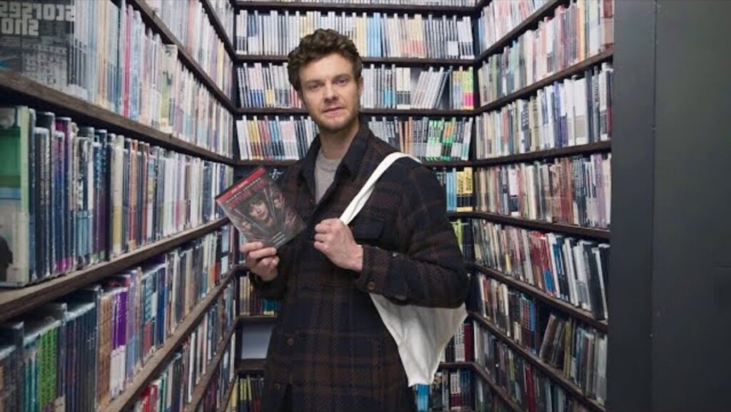 Jack Quaid in the Movie Closet with a copy of Madame Web in a Happy, Sad, Confused podcast skit.