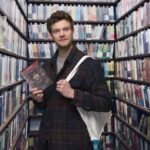 Jack Quaid in the Movie Closet with a copy of Madame Web in a Happy, Sad, Confused podcast skit.