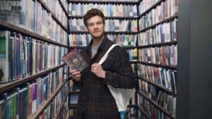 Jack Quaid in the Movie Closet with a copy of Madame Web in a Happy, Sad, Confused podcast skit.