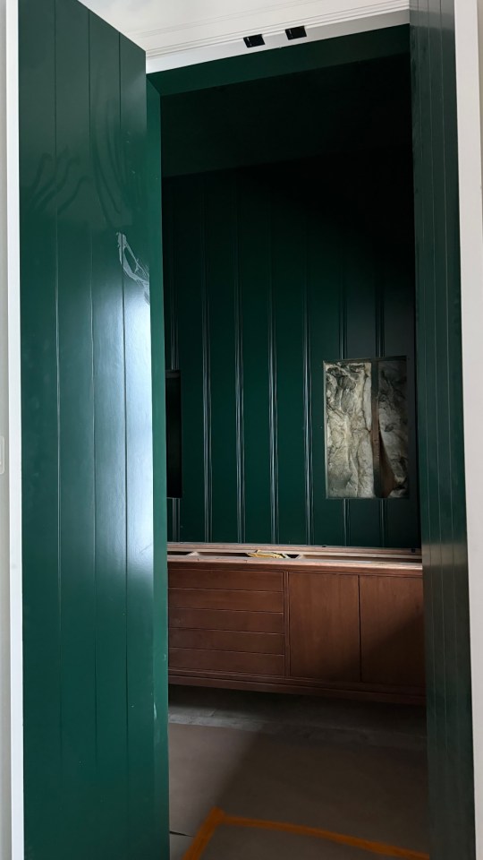 Interior of a room under construction with dark green walls and a wooden cabinet.