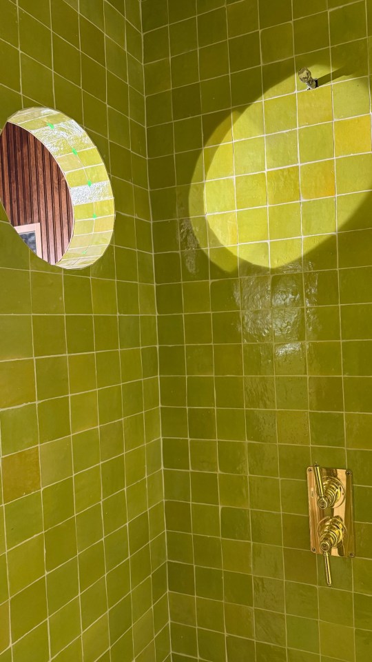 Green tiled shower with brass fixtures and arched window.