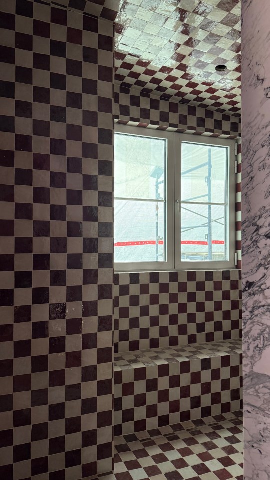 Green tiled shower with gold fixtures and arched window.