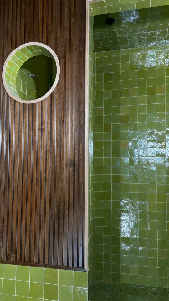 Green tiled shower with wood paneling.