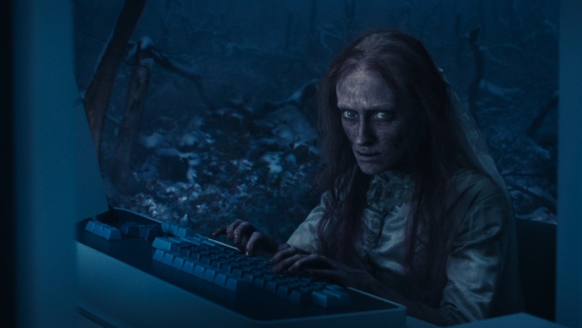 A small woman who looks like a demon working at a computer int he dark forest on Severance