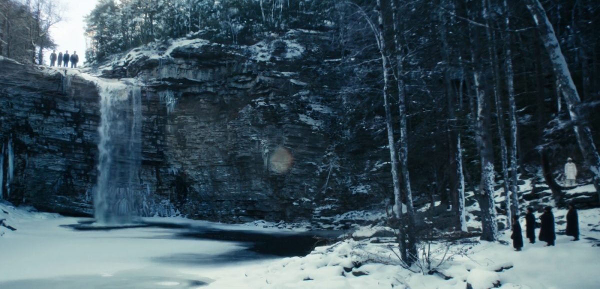 Four people stand atop a small waterfall while five looks on from the snow-covered woods on Severance