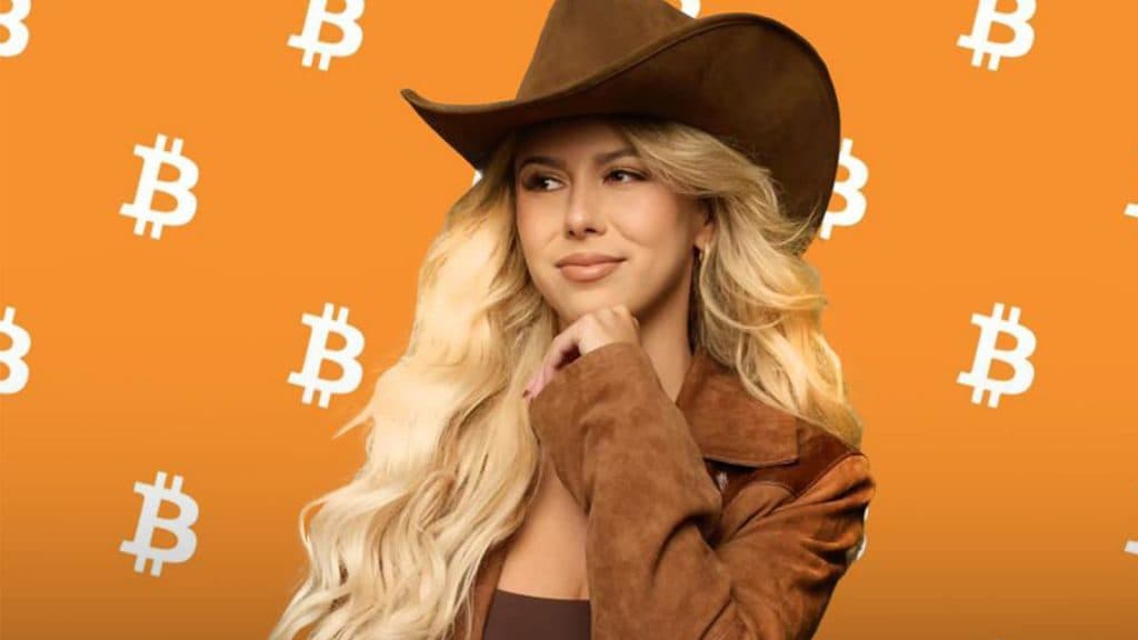 Haliey Welch wears a cowboy hat against a background of bitcoin symbols.