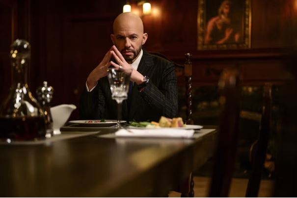 Lex Luthor seated at a table, hands clasped.