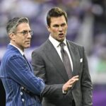 Kevin Burkhardt and Tom Brady stand next to each other on a field.