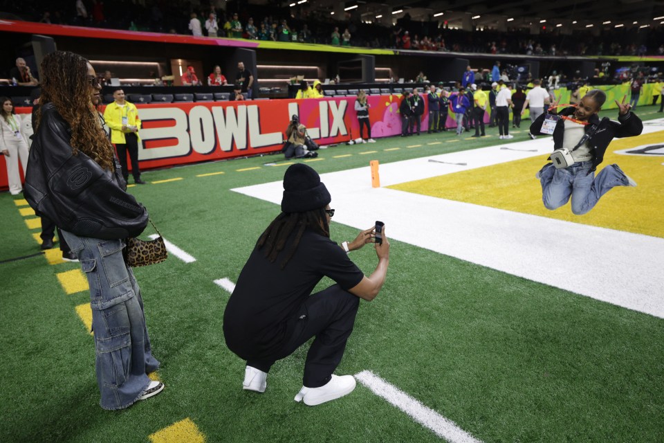 Jay-Z photographing his daughter on a football field before a game.