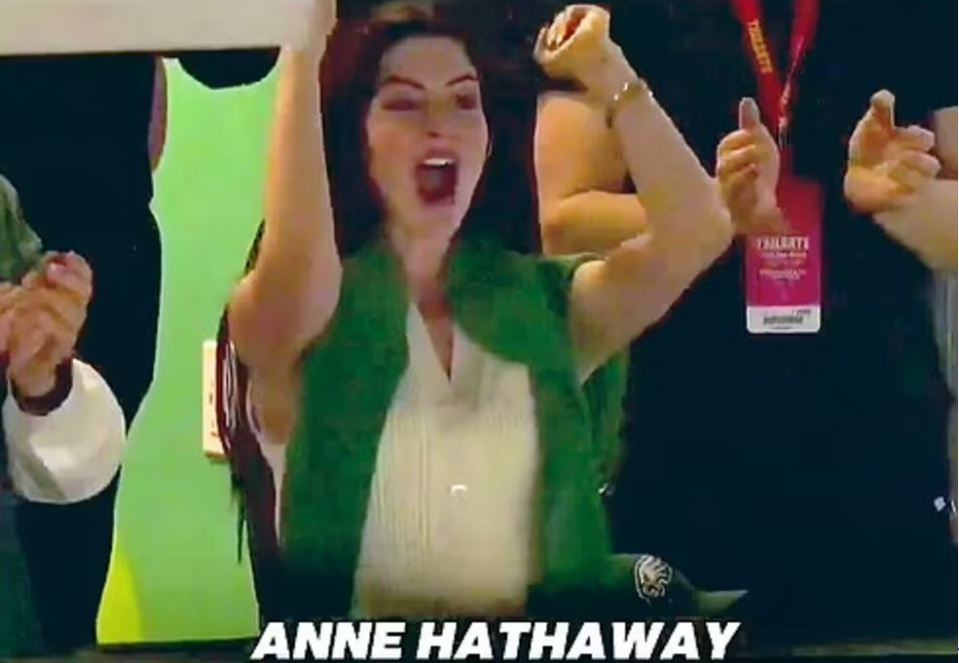 Anne Hathaway celebrating enthusiastically on a Jumbotron.