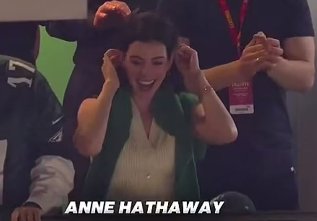 Anne Hathaway laughing with hands over her ears.