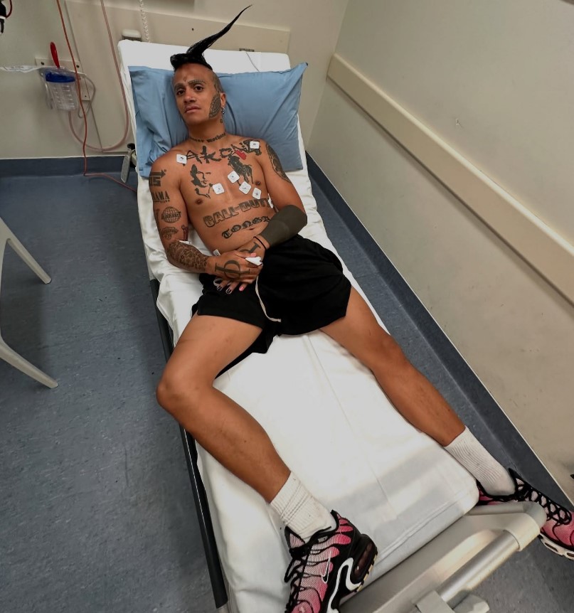 A tattooed man lying on a hospital bed.