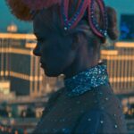 A woman in a glitzy costume and headdress with the lights of Las Vegas in the background