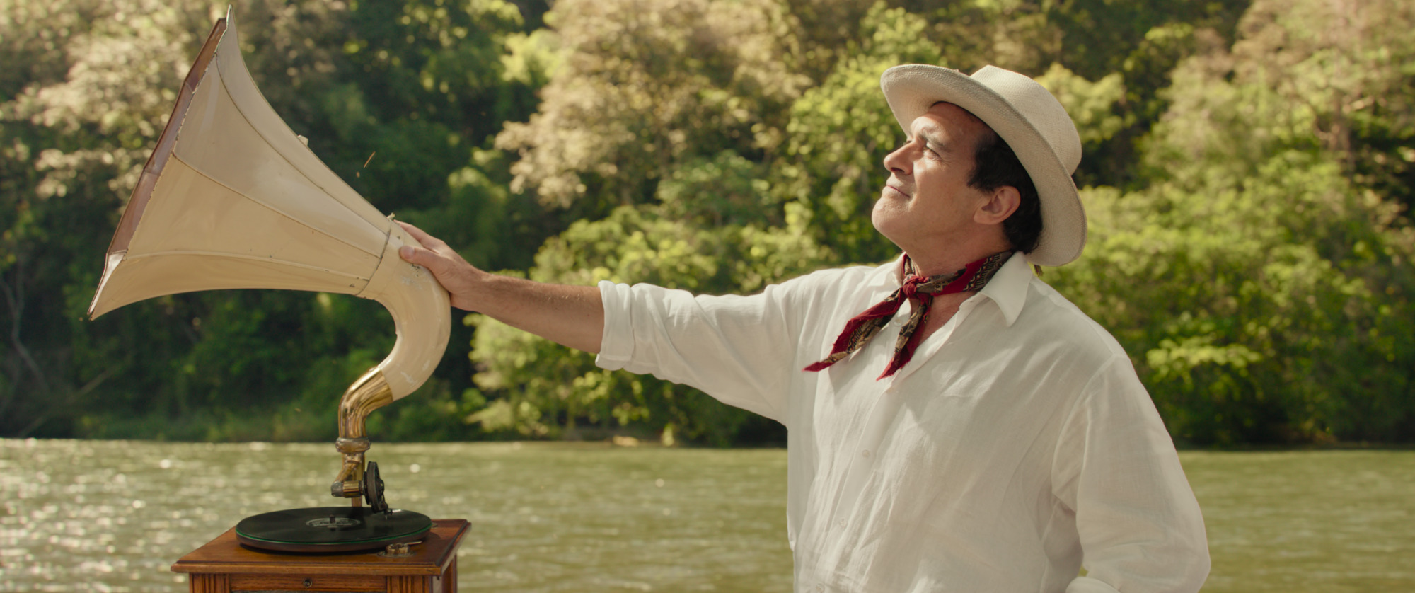 Antonio Banderas as a riverboat captain, one hand on a phonograph, as he squints into the sunlight from Paddington in Peru