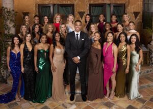 A crowd of women in gowns stands around a man in a black suit and tie