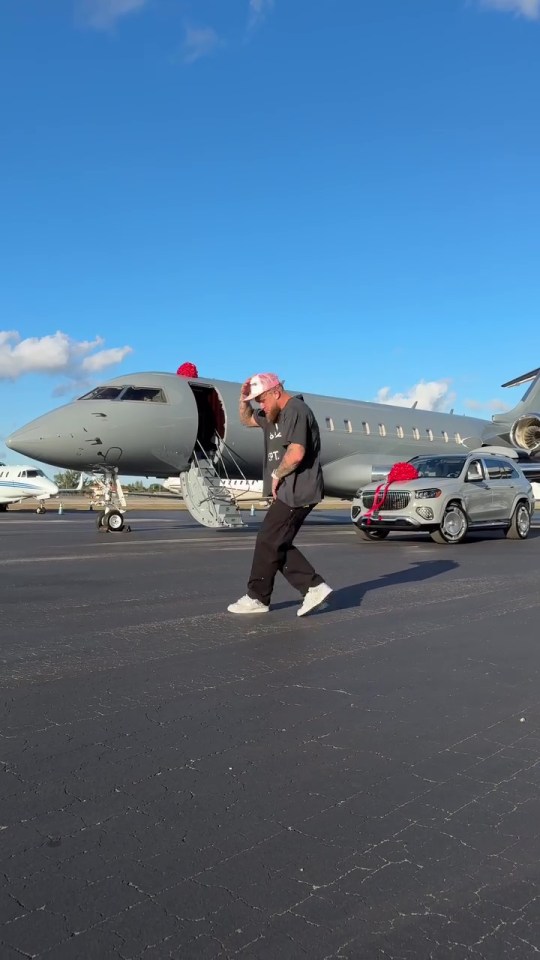 Man walking on tarmac in front of a private jet and luxury SUV.